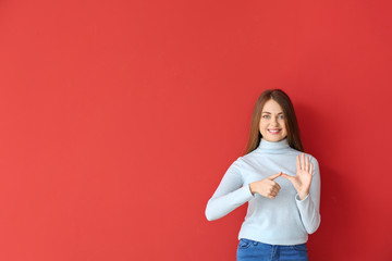 Young deaf mute woman using sign language on color background