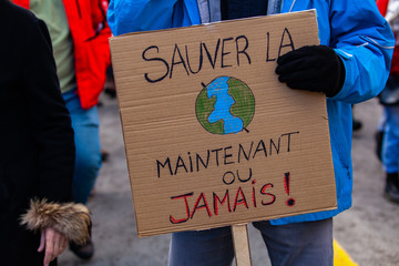 Environmentalist holds poster at rally. A French sign reads save it now or never and depict planet...