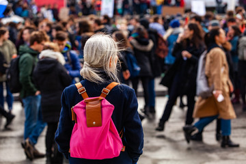 Person watches ecological protest. An older woman is viewed from behind, wearing a pink shoulder...