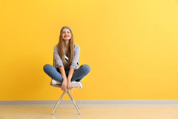 Happy young woman sitting on chair near color wall