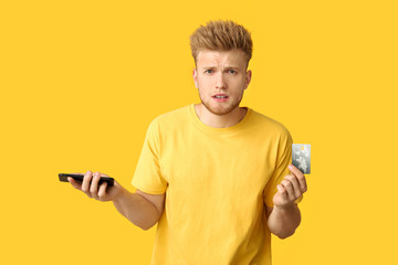 Stressed young man with credit card and mobile phone on color background