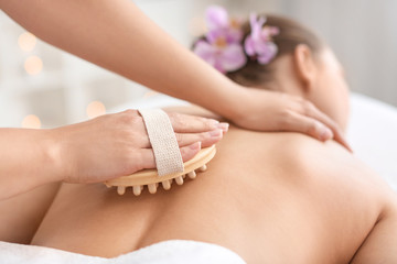 Beautiful young woman receiving massage with brush in spa salon