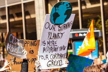 Homemade sign at environmental rally. A cardboard sign is viewed close up, saying our burning planet is more important than your corporate greed, as activists march against climate change