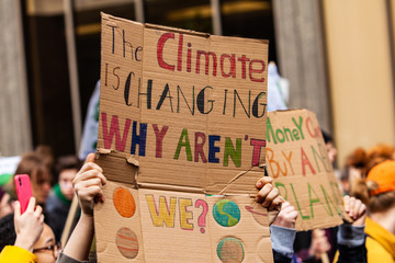 Homemade sign at environmental rally. A colorful cardboard placard is viewed close up, saying the climate is changing, why aren't we, in the hands of ecological activists as they protest in the city - obrazy, fototapety, plakaty