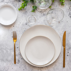 Elegant table setting, white plate with gold cutlery and wine glasses on cement background. Scandinavian style