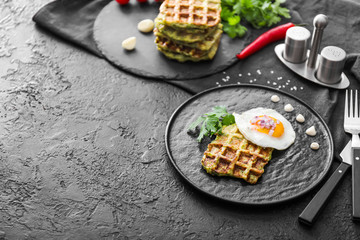Plate with tasty squash waffle and fried egg on dark table
