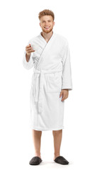 Handsome young man in bathrobe drinking coffee on white background
