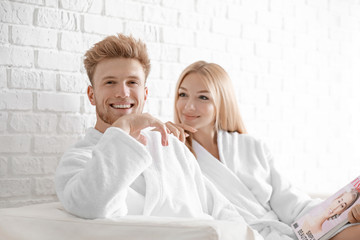 Happy young couple in bathrobes sitting on sofa at home