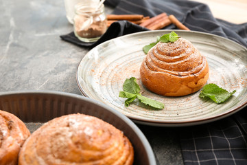 Plate with tasty cinnamon bun on grey table