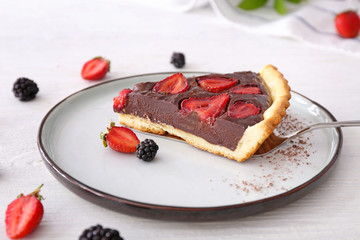 Plate with piece of tasty chocolate strawberry cake on white table