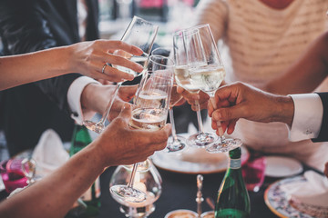 Luxury christmas celebration. People hands toasting with champagne glasses at delicious feast outdoors in the evening. Family and friends clinking glasses and cheering with alcohol - obrazy, fototapety, plakaty