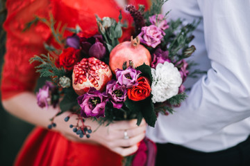Wedding asymmetrical stylish bouquet with red roses and pomegranate.