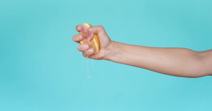 Squeeze the juice out of the lemon by hand, squeeze out half the yellow lemon by hand. Close-up. Slow motion. Turquoise background.