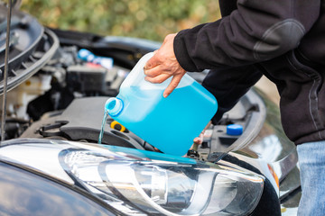 man refills windshield wiper water on a car