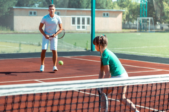 Father wearing white t-shirt and shorts playing tennis with his girl
