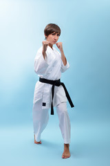 Young karate woman in a white kimono with black belt demonstrates fighting stances and strikes. Girl at studio shows martial arts