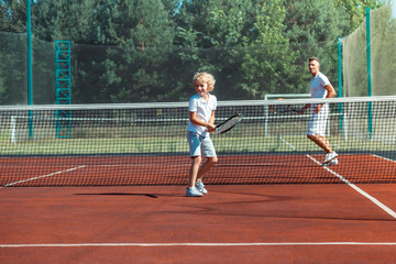 Curly son laughing while playing tennis with daddy