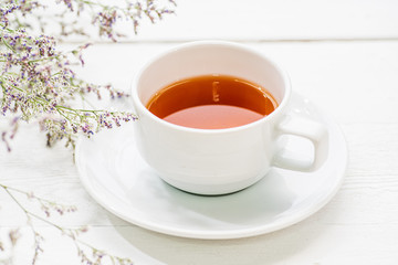 A cup of tea on white painted wood background with branch of small flower
