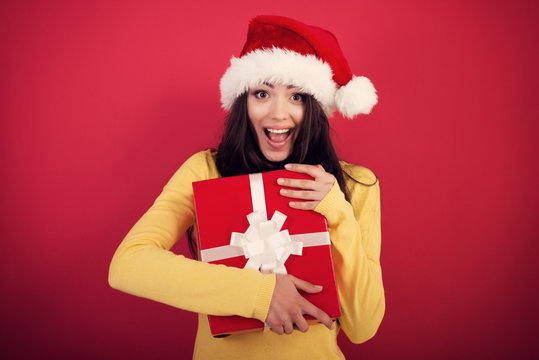 Christmas girl. Young pretty smiling woman holding gift box, isolated on red background, new year and x-mas holiday concept, image toned