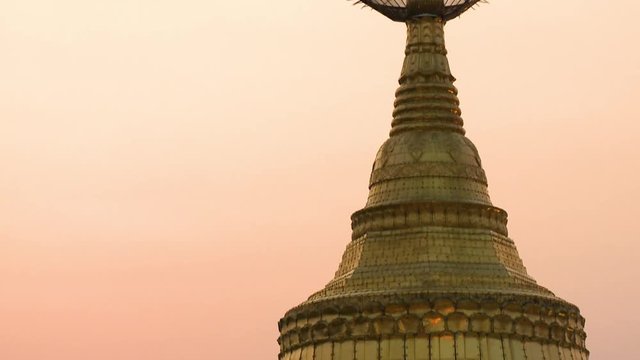 Handheld, tilting, medium close up shot of The Kyaiktiyo Pagoda sitting on top of Golden Rock.