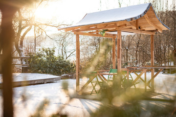 Beautiful wooden small fairy elf arbor gazebo in the sunlight dawn's sunshine in winter snow