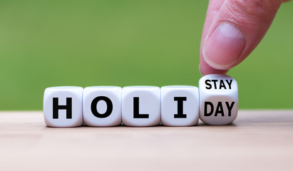 Holiday at home concept. Hand turns a cube and changes the word "holiday" to "holistay".