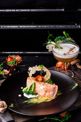 Beautiful serving of baked salmon with creamy sauce with broccoli tomatoes on black matte plate on rustic wooden tray