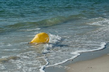 closeup of yellow buoy in the water oin the beach