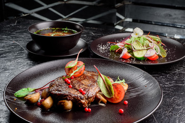 grilled juicy steak with grilled mushrooms, tomatoes and cranberries on a dark round plate
