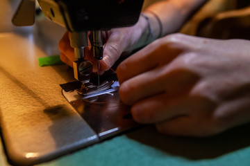 Fototapeta na wymiar Young fashion designer changing thread. Hands of a young dressmaker are seen close up, replacing red thread on an industrial sewing machine. Awkward task before stitching fabric with machinery.