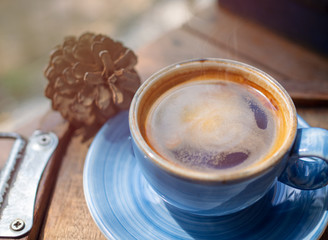 Hot American coffee is in a blue ceramic solution placed on a wooden floor table in cafe with smoke and sunlight.Coffee break in morning/ selective focus