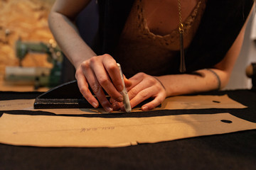 Fashion designer marking sewing patterns. Skilled dressmaker is viewed closeup, using tools to cut shapes from fabric. Pattern of a new dress laid out on work surface in atelier.