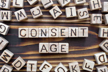 consent age wooden cubes with letters, sexual education concept, around the cubes random letters, top view on wooden background