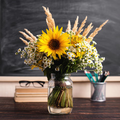 Glasses teacher books and wildflowers bouquet on the table, on background blackboard with chalk. The concept of the teacher's day. Copy space.