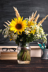 Glasses teacher books and wildflowers bouquet on the table, on background blackboard with chalk. The concept of the teacher's day. Copy space.