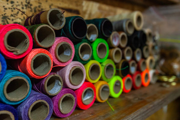 Colorful threads on a shelf in workshop. A close-up view of many colored thread spools stored on shelving inside a dressmakers studio. Cardboard rolls of threads shot on a slight angle with copy space