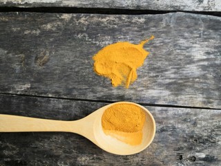 Turmeric powder on a wooden spoon on an old black plank floor