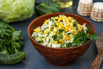 Healthy salad with cabbage, cucumbers, corn and parsley in a salad bowl on a dark background, horizontal photo