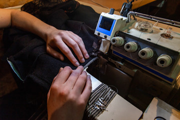 Fashion designer using vintage overlock. Hands of a seamstress are seen using an overlock machine inside her workshop. Overlocking pieces of fabric during clothes development.