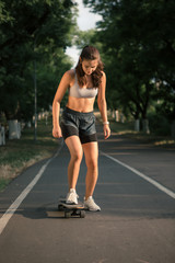 Portrait of a young brunette woman skateboarding on a road in the park.