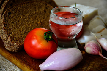  Freshly baked bread on a wooden cutting board with bacon, tomatoes, onions, garlic, basil and a shot of vodka