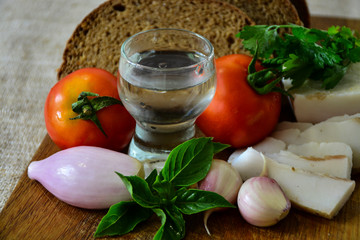  Freshly baked bread on a wooden cutting board with bacon, tomatoes, onions, garlic, basil and a shot of vodka