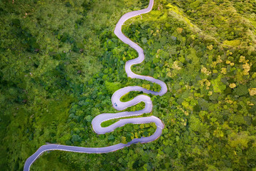 Aerial view of cars driving on curved, zigzag road or street on mountain hill with green natural forest trees in rural area of New Taipei City, Taiwan