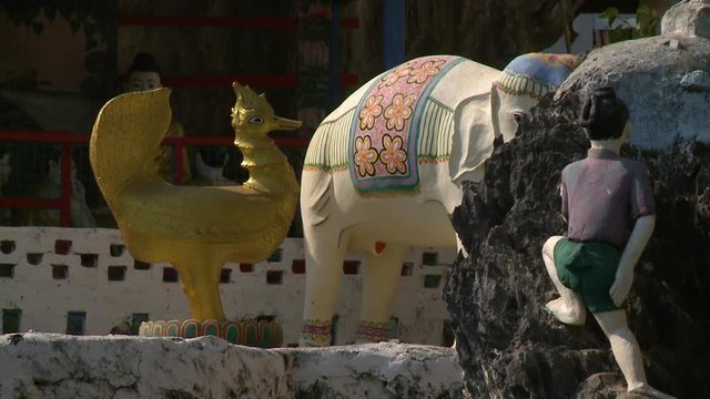 Steady, medium close up shot of statues of a golden chicken, painted elephant and a child.