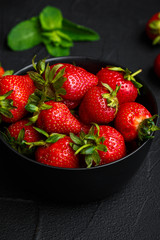 Heap of fresh strawberries and mint leaves in black bowl on dark background. top view
