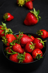Heap of fresh strawberries and mint leaves in black bowl on dark background. top view