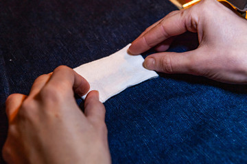 Placing white patch on blue jean fabric. Hands of a young dressmaker are seen close-up, preparing a blank label on blue denim fabric. Designer finishing authentic handcrafted product.