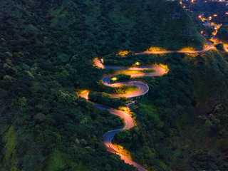 Aerial view of cars driving on curved, zigzag road or street on mountain hill with natural forest...