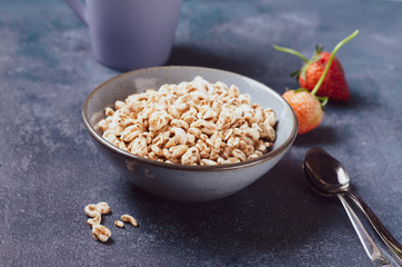 Organic puffed spelt wheat in blue bowl with milk and strawberry for breakfast.