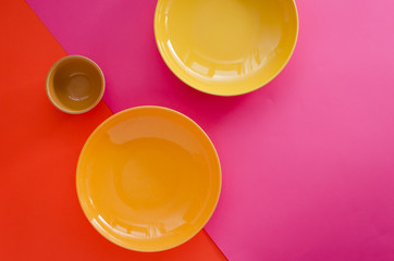 Fototapeta na wymiar Empty yellow plates and bowl on bright pink orange colored background